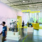 Colour photograph of a bright exhibition space with display objects and visitors