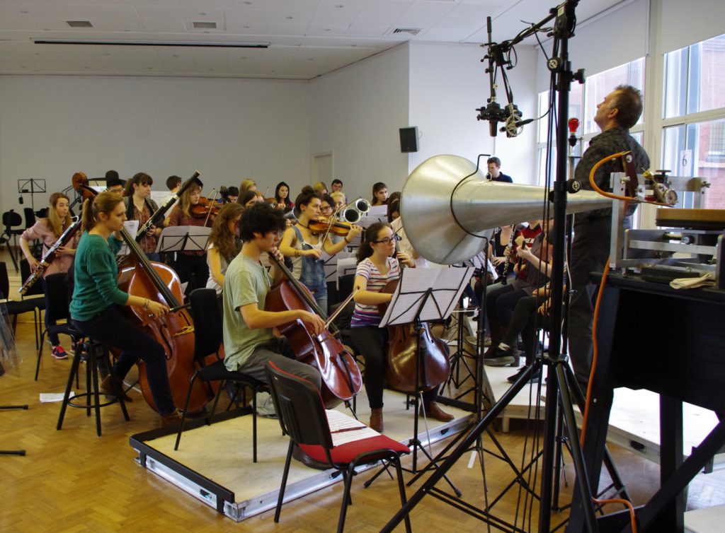 Colour photograph of the cellos and basses part of the royal college of music chamber orchestra recording music to wax discs