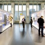 Colour photograph of a bright exhibition space with display objects and visitors