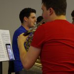Colour photograph of a member of RCM playing the french horn with the conducting being done via a tablet computer