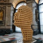 Colour photograph of a wood and bronze sculpture of a stylised human head