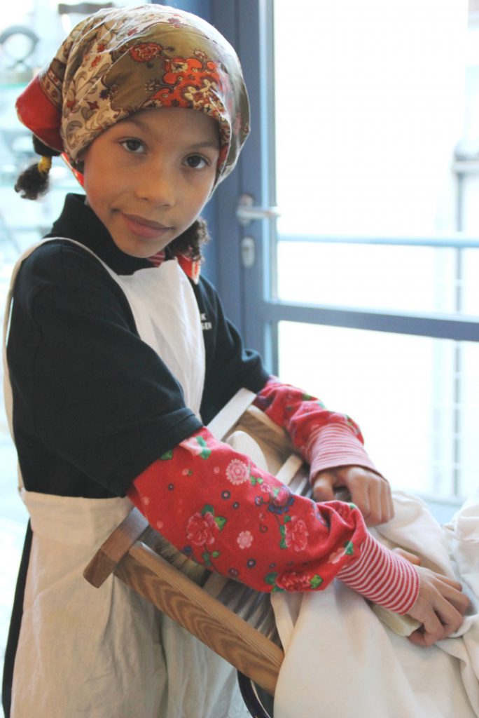 Colour photograph of a young girl demonstrating the use of a clothes washing board