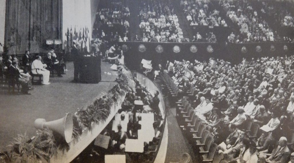 Black and white photograph from the World Power Conference of a large stage with seated presenters and a large seated audience