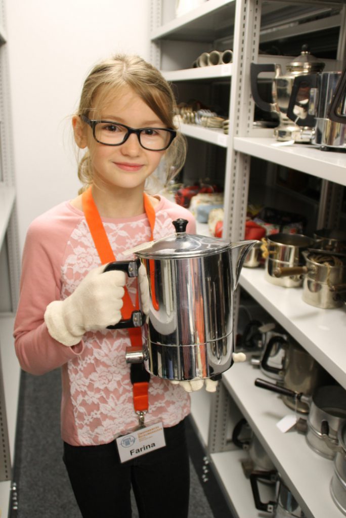 Colour photograph of a young girl holding an early metal kettle