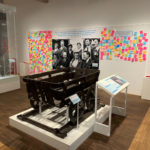 Colour photograph of a coalmining cart displayed in front of Margaret Thatcher's photograph in an exhibition gallery