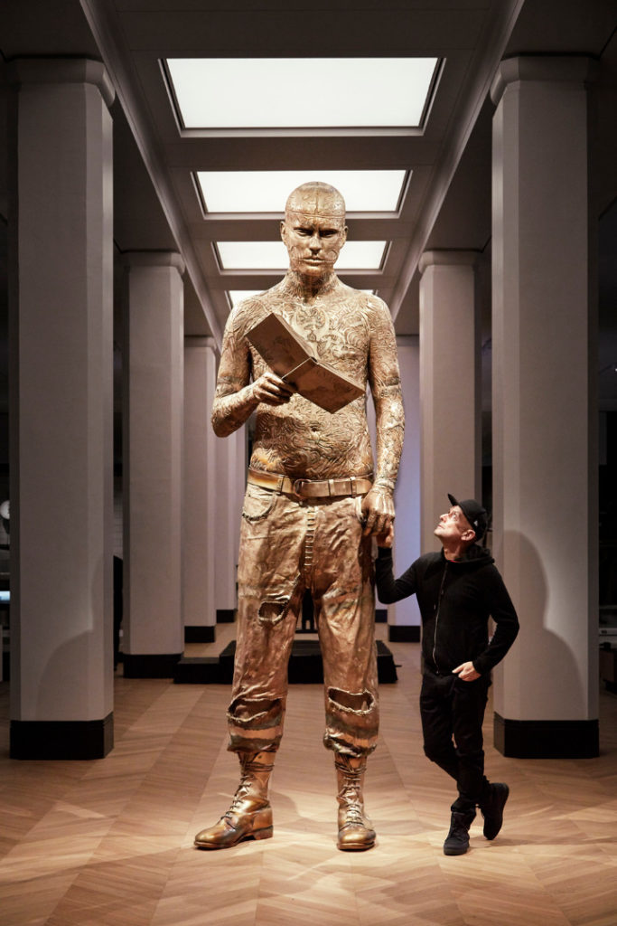 Colour photograph of the Self Conscious Gene sculpture situated on gallery with artist Marc Quinn