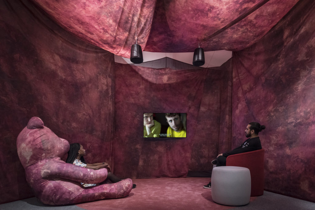 Colour photograph of attendees viewing a video in the Oreet Ashery exhibition