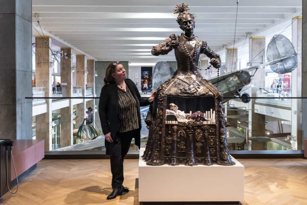 Colour photograph of the Santa Medicina sculpture situated on gallery with artist Eleanor Crook