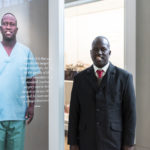 Colour photograph of a man standing alongside his on gallery portrait
