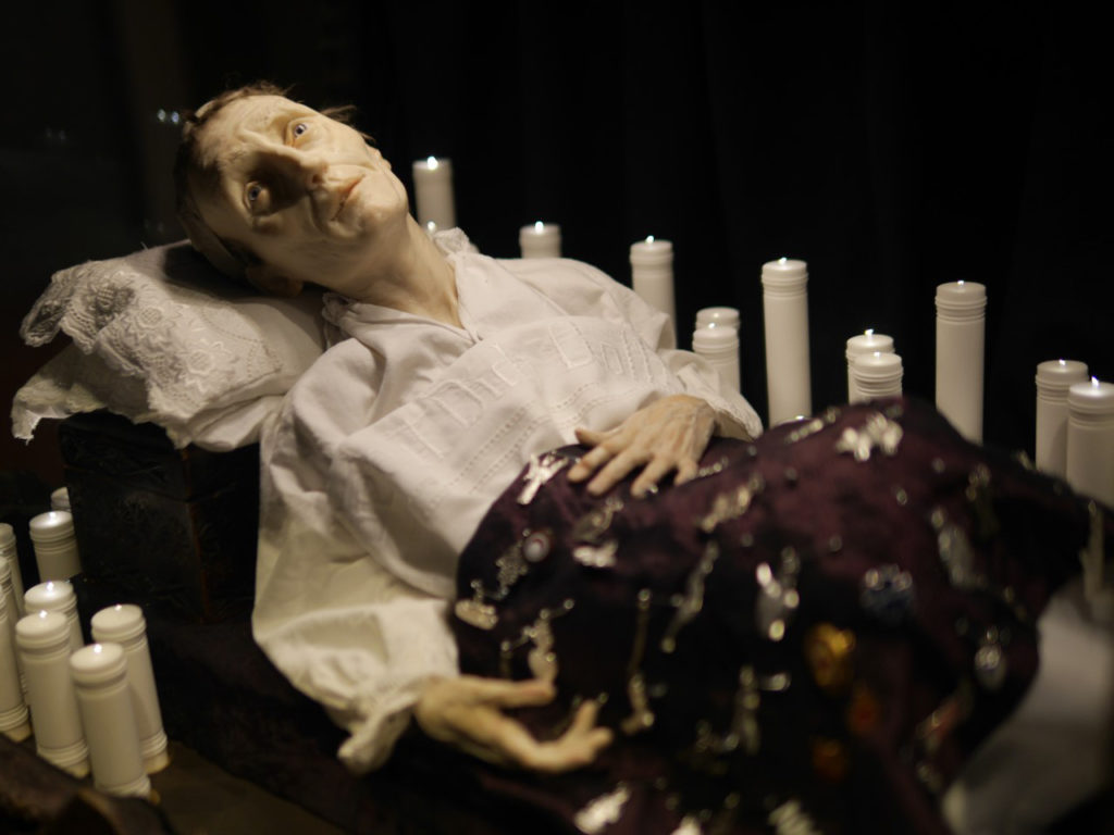 Colour photograph of a sickly wax figure and candles within the Santa Medicina sculpture