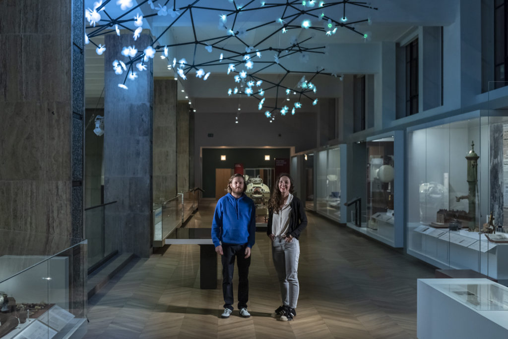 Colour photograph of the artists beneath the Bloom light installation
