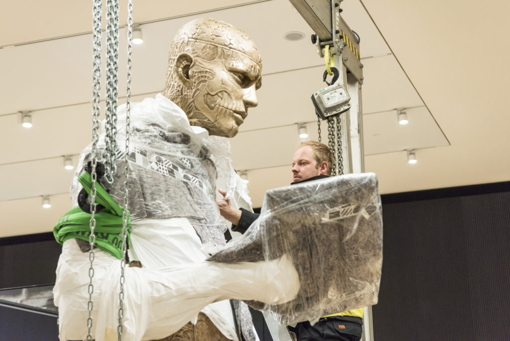 Colour photograph of a large human sculpture wrappend in cellophane for transportation