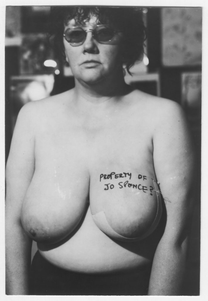 Black and white photograph of a topless Jo Spence with Property of Jo Spence written across her breast