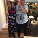 A woman holds up a dress stitched with the slogan My Mind My Body My Choice