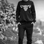Black and white photograph of someone wearing a sweatshirt with a stylised Transformer logo in the shape of a uterus