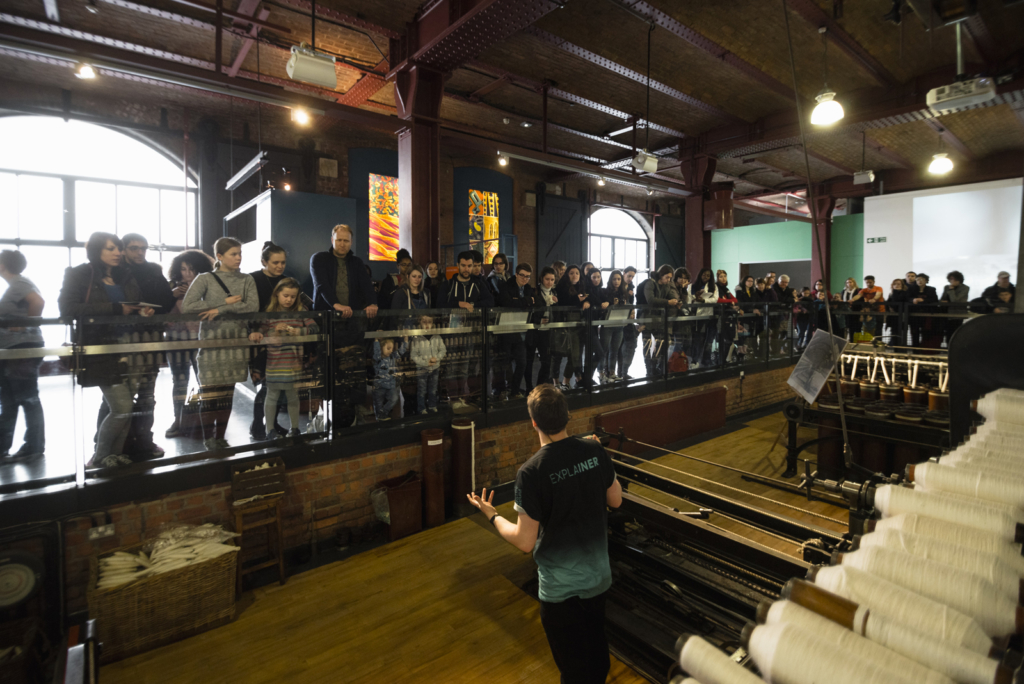 Colour photograph of an explainer talking to a museum audience about a weaving machine