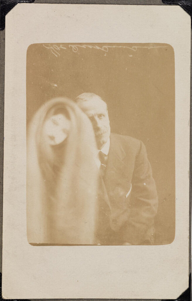 Sepia photograph of a seated man showing a spectral figure to his right