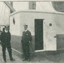 Black and white photograph of two naval staff outside a wireless station on board a ship