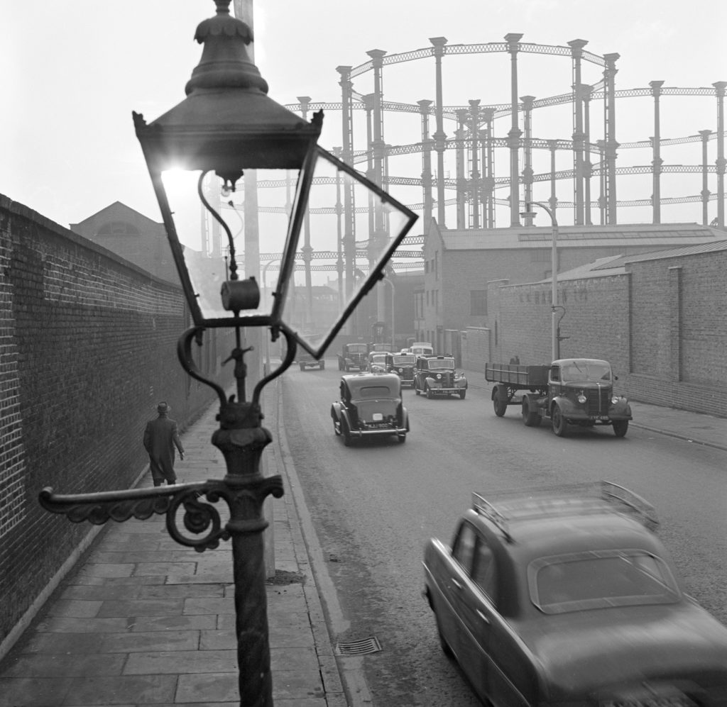 A street view with an open gas street light and the gasometers at kings cross in the distance imperial gas light and coke company gas holders greater london camden town