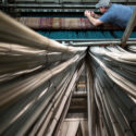 Photograph of a weaver mending a broken thread inside a giant broad loom