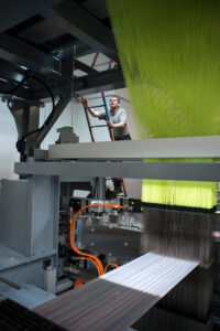 Photograph of a man preparing a weave on a new multi shuttle Jacquard loom