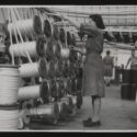 Black and white photograph of a woman working at a weaving machine