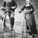 Monochrome photograph of a man and a woman riding penny farthing bicycles